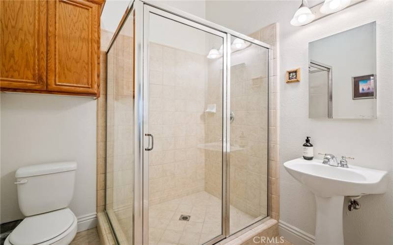 Extensively tiled bathroom offers a glass enclosed shower and pedestal sink.