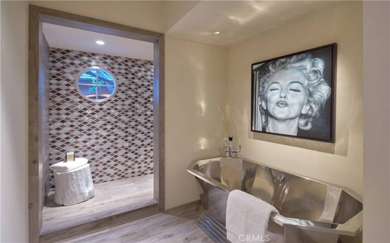 Stainless steel soaking tub located in secondary bedroom, with custom tile in open shower.
