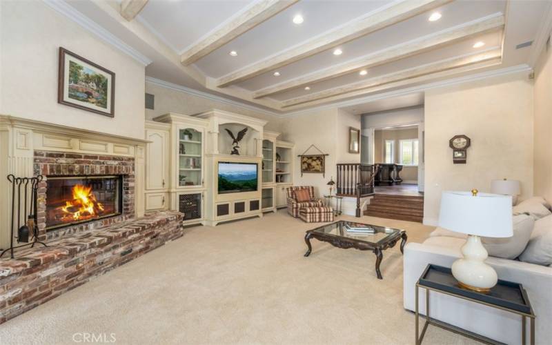 Large Family room with custom built-ins, recessed lighting, custom brick fireplace, beamed ceilings with double doors leading to the beautiful backyard.