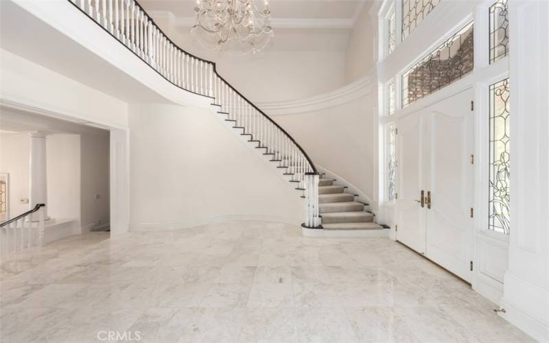 The spectacular double door foyer entry with its whimsical spiral staircase is accented with high soaring ceilings, oversized custom crown moldings, crystal chandelier, marble, stone, and designer accents.