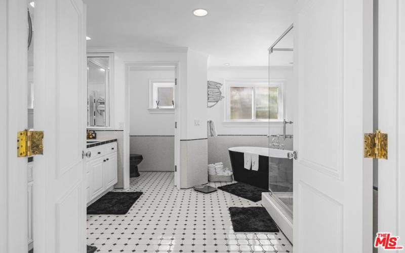 bathroom is complete with a long countertop two sinks, large mirrors throughout, standing shower, elegant tub, and separate toilet room