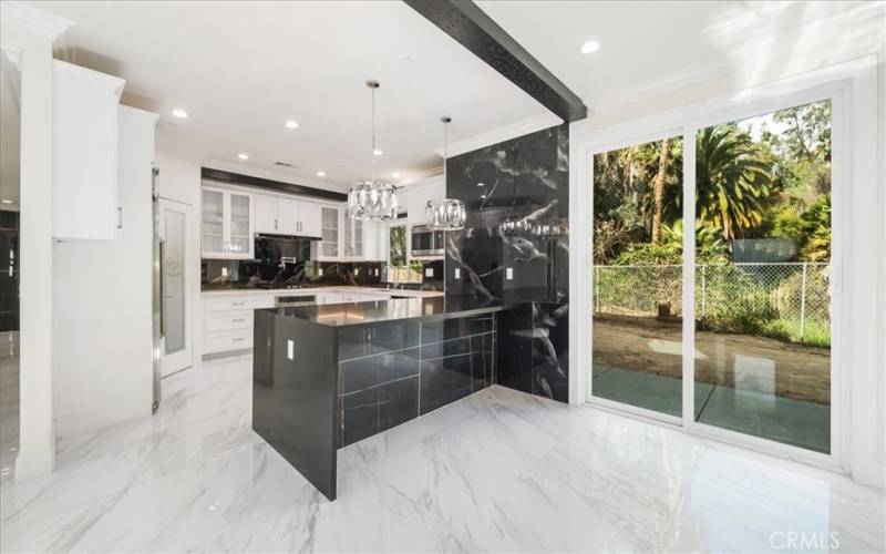 Modern kitchen with radiant porcelain tile flooring and a quartz-topped island, complemented by white storage cabinets and sleek dark accents. Natural light enhances the space, while sliding glass doors offer a glimpse of the outdoors