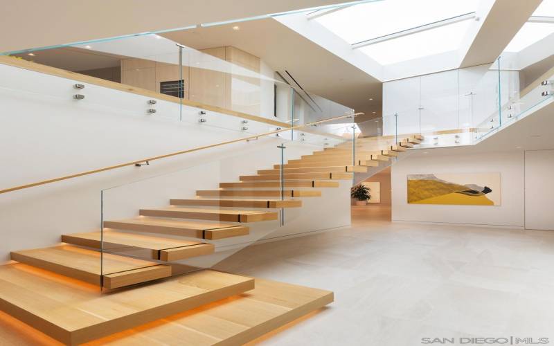 Grand two story foyer and rift oak floating staircase bathed in light from huge trapezoidal skylight