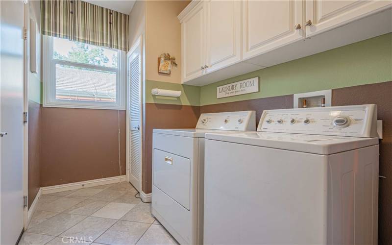 Laundry room has washer/dryer that are staying with built-in white cupboards above with stainless steel knobs. Tiled flooring. Door to the right is the entrance to the garage. Door to the left is your water heater.