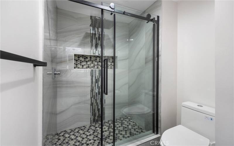Primary bathroom has a custom shower with rainfall showerhead and beautiful black hardware frame.