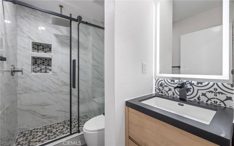 Hall bathroom has a floating vanity, custom tile backsplash, a sleek toilet, and designer mirror with WiFi and backlighting.