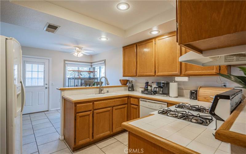 Your kitchen is tiled flooring with oak cabinets. White tiled countertops. On the far left side is kitchen nook space for another table. The door here leads to the outside concrete pad which is great for outdoor entertaining!