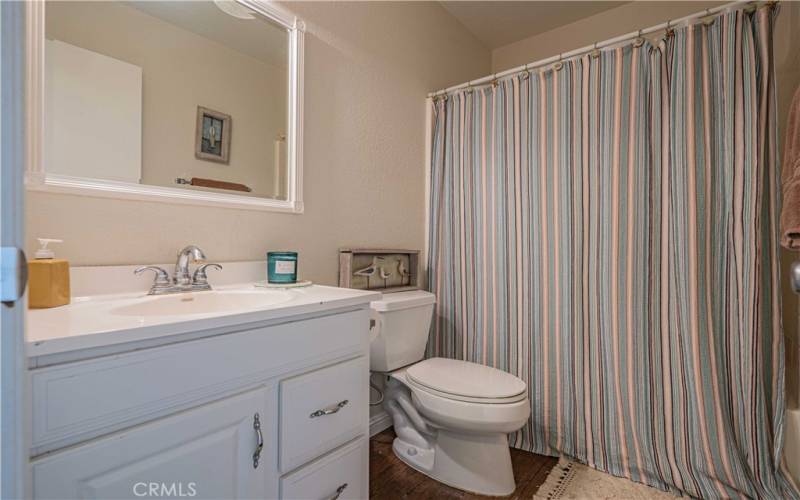 Hallway bathroom is tiled with a white sink vanity, mirror and lights above. Toilet. Tub/shower combination.