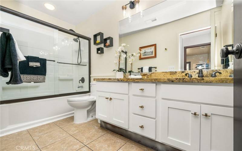 Upstairs hall bath features tile floors, fresh white shaker cabinetry with marble counter and dual vanity sinks. Bath services both middle bedroom and loft.