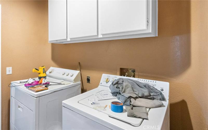 Laundry room is off of the garage and features a sink and additional cabinets and storage opposite the machines