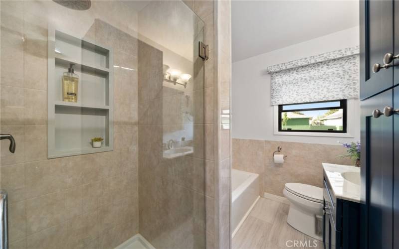 A fully renovated bathroom featuring a separate tub and a newly tiled shower with a modern glass door + extra cabinets to store linens.