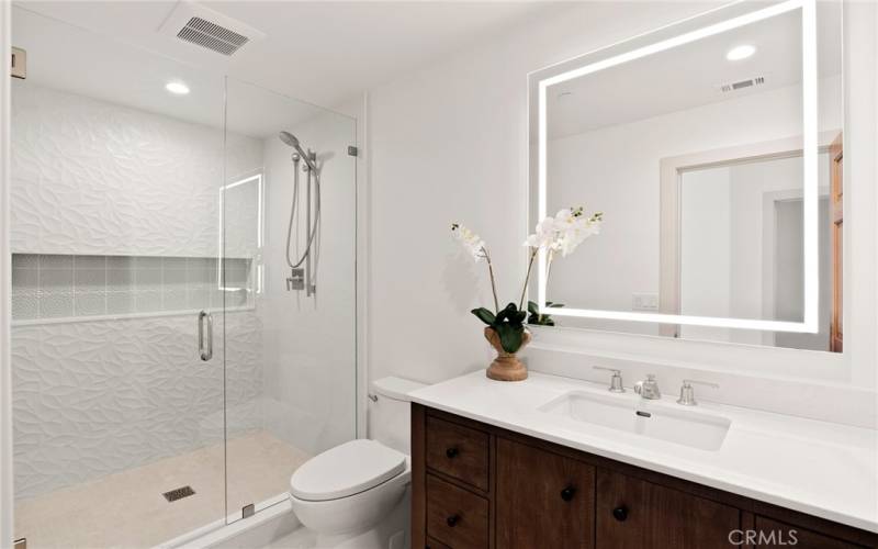 Completely remodeled bathroom with lighted mirror and contemporary vanity with quartz countertop.