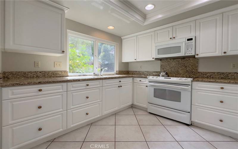 Large working kitchen with lots of granite counters and storage space, microwave, electric cooktop, recessed lighting and more.
