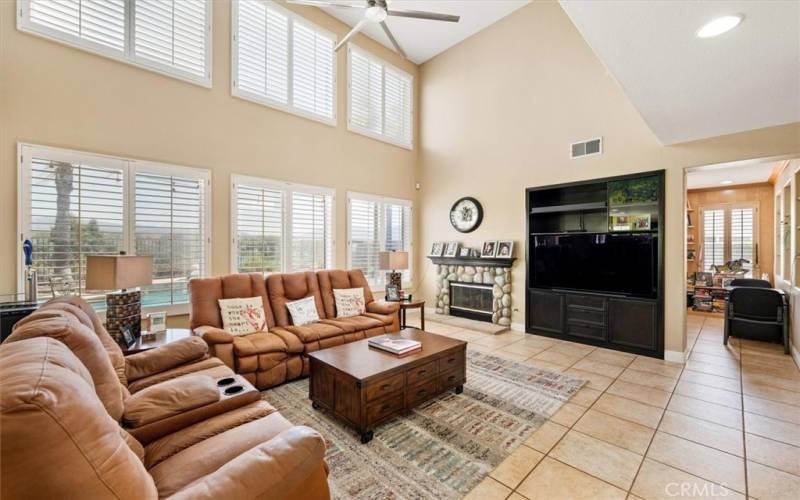 Spacious family room with stone fireplace, shutters, custom tile floors and dramatic high ceilings