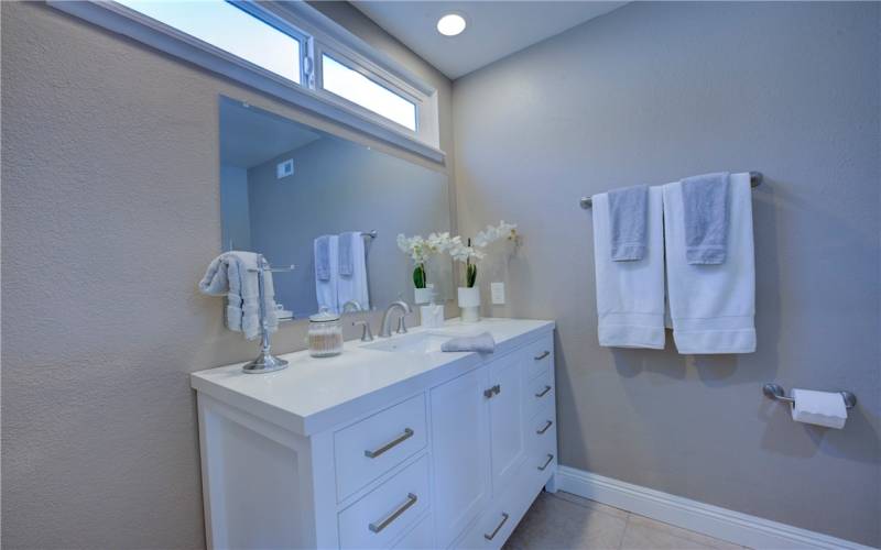 The primary bath white cabinetry with quartz counter top. Note the window above the mirror for natural light.
