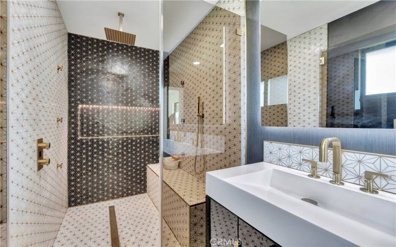 Bathroom 1 with dual vanity, hexagonal tile, floating toilet, and designer shower with gold-trimmed tile and triple function rain, handheld shower heads and body sprays