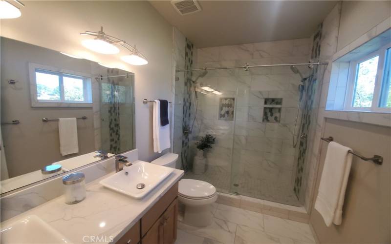 View of private primary bathroom with Quartz counter, double sinks, custom tiled walk-in shower.