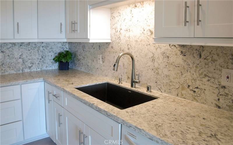 A large kitchen sink with a pull-down faucet and soap dispenser. Quartz countertop and full quartz backsplash.