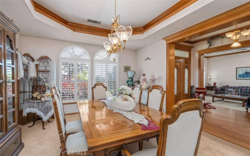 Dining room with tray ceiling and bright natural light.  Look at the solid wood trim, leaded glass entry door and transom in the entry to the right of the photo.