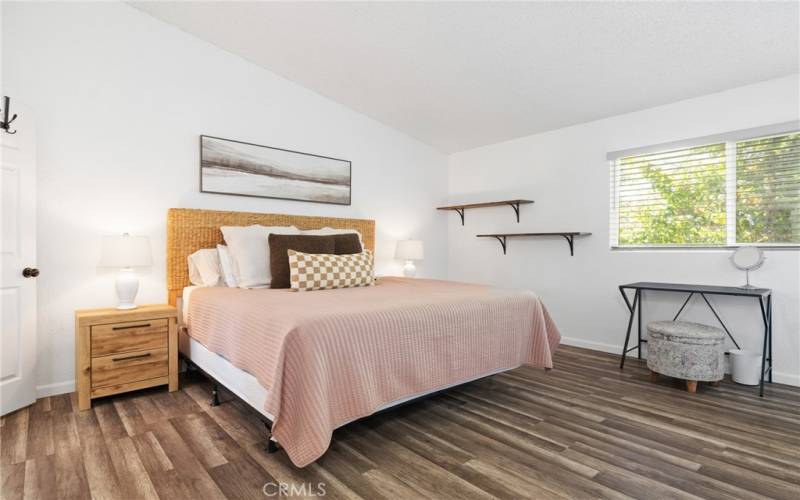 The primary bedroom features laminate wood floors and vaulted ceilings.