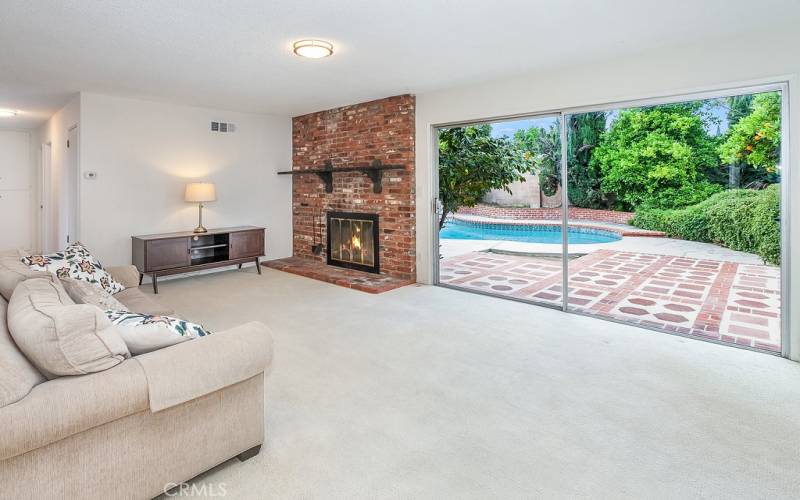 The freshly painted living room with wall-to-wall Berber carpet is bathed in natural light and is enhanced by a floor-to-ceiling brick fireplace with mantle and sliding glass door that leads to the expansive backyard and pool.