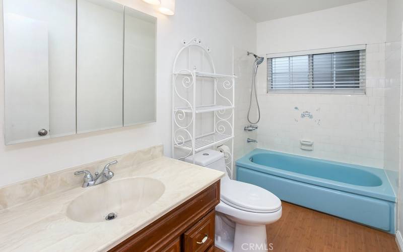Full bathroom is freshly painted with wood-grained vanity, mirrored medicine cabinet, new light fixture, tiled tub/shower, privacy window, and wood laminate floors.