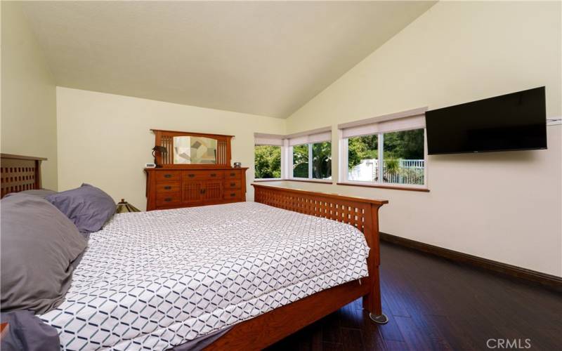 Large primary bedroom with windows all around and high ceilings. REAL hardwood floors!