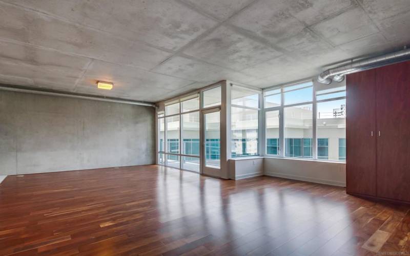 Open floor plan loft living/dining/home office/bedroom area. The bedroom area has two custom-curated, hard-wood closets for hanging clothes and drawers. Floor-to-ceiling glass walls & door opening to private balcony, exposed a/c ducts& accent cement walls