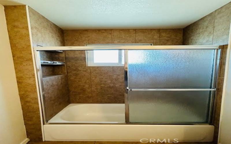 Tiled bathtub/shower combo with built in shelves.