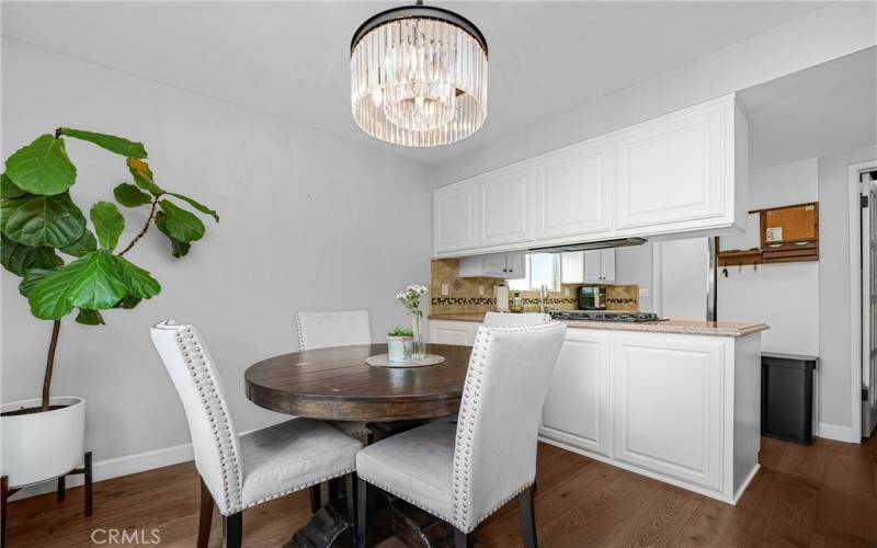Step into a cozy dining area enhanced by natural light and a chic chandelier. The open-concept kitchen, with sleek white cabinetry and modern fixtures, provides the perfect backdrop for home-cooked meals and entertaining guests.