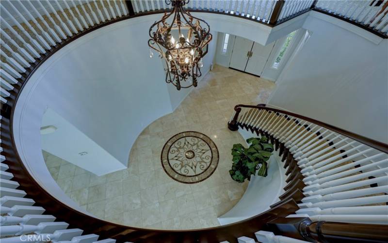 Stunning view of the grand foyer with circular staircase and dynamic chandelier from upstairs.