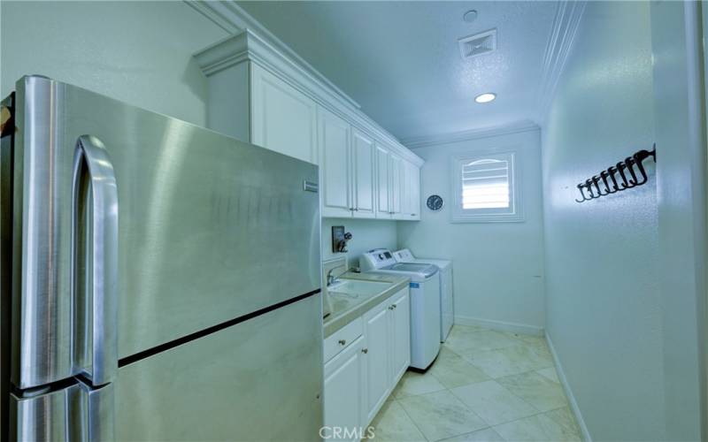 Spacious laundry room has a sink, a window and space for an extra refrigerator.