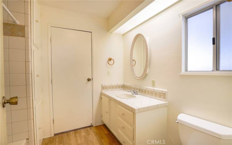 The main bathroom features laminate wood floors, large vanity, linen cabinet and a tub/shower combination with tile surround.