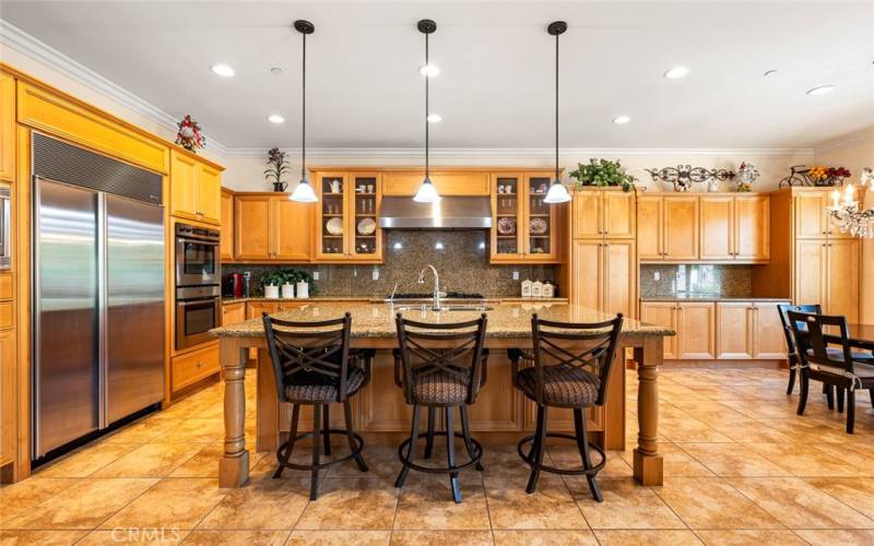 Gourmet kitchen with granite countertops, center island with bar seating, breakfast nook, and premium stainless steel appliances including SubZero built-in refrigerator, double ovens, kitchen hood, dishwasher and built-in microwave.