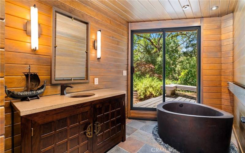 The unique primary bathroom has a distinctive vanity with concrete countertop, sliding glass door and a Japanese style copper soaking tub that fills from the ceiling.