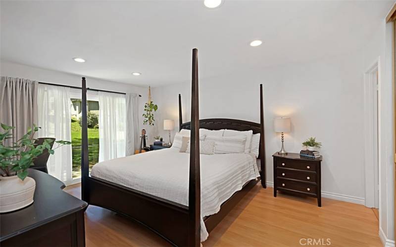 The primary bedroom is generously spacious, featuring laminate flooring and recessed lighting that create a cozy and modern atmosphere. It offers direct access to the lush and green back patio area, perfect for relaxing and enjoying the outdoors right from your own retreat.