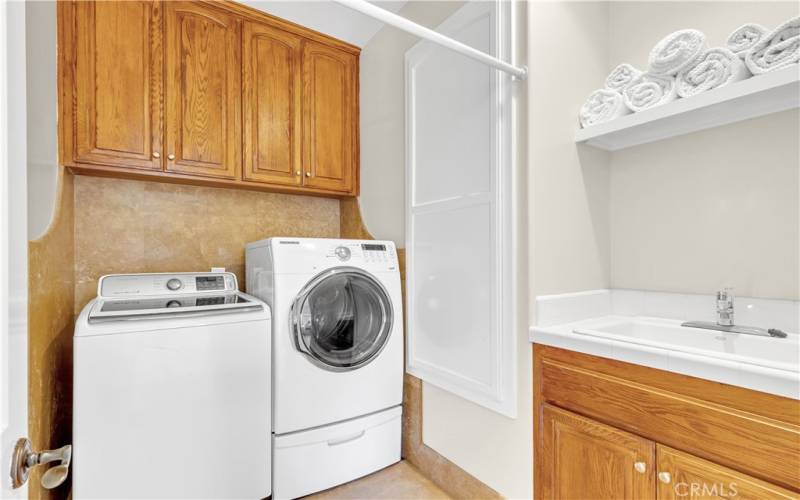 Upstairs laundry with travertine walls and flooring is a plus with storage and a sink.