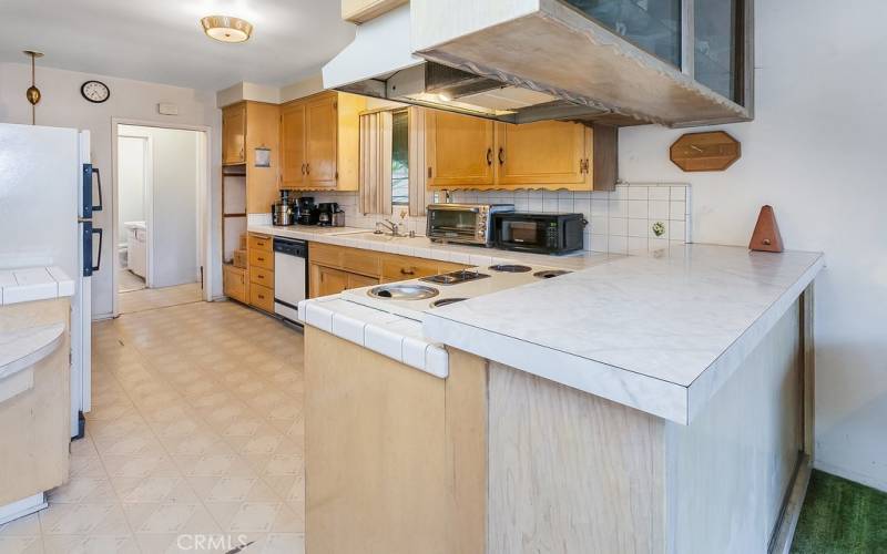 The cook in the family is going to appreciate the galley kitchen with its large window, rich wood-grained cabinetry that reaches the ceiling, tiled countertops, dual basin sink, electric cooktop with ventilation hood, dishwasher, convenient breakfast bar and easy-care floors.