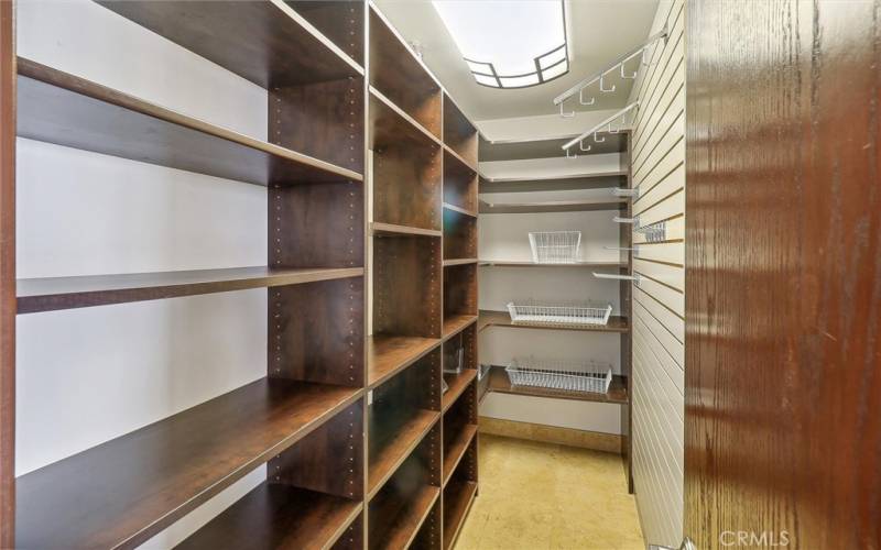 Large walk-in pantry with custom shelving and wall slats with accessories hooks and baskets.