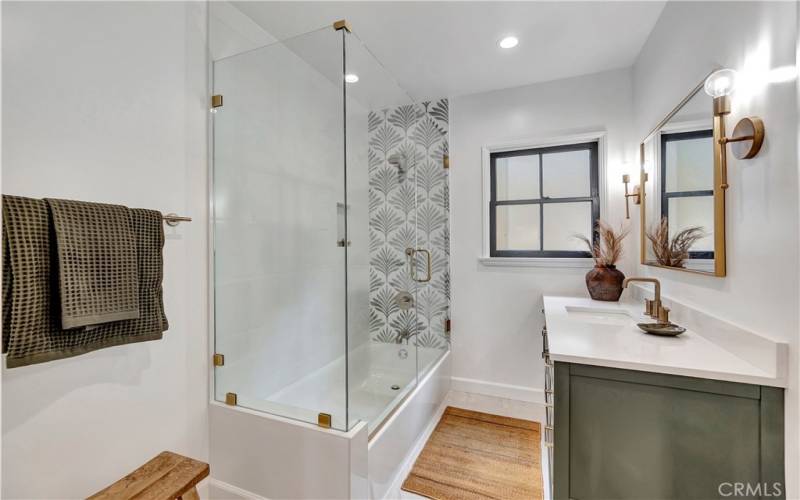 Bathroom with brushed gold hardware, quartz counter, botanical tile and frameless glass shower