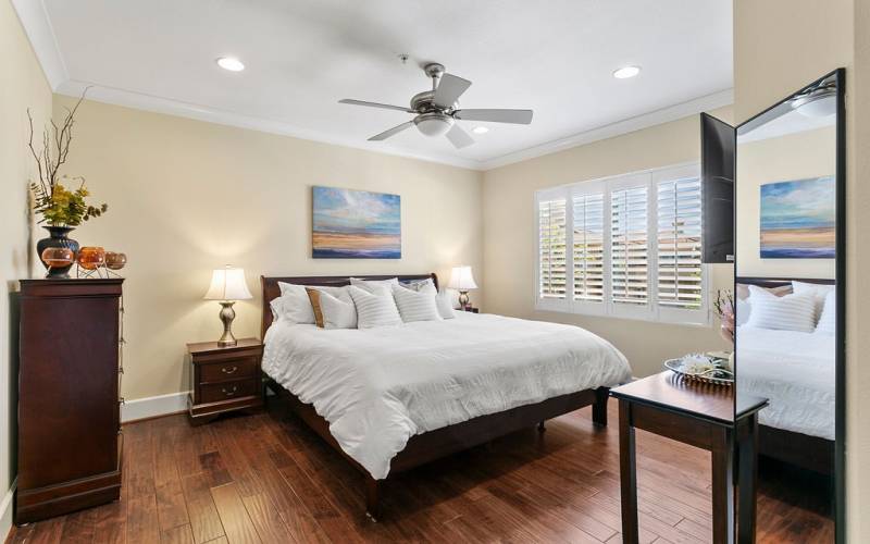 Elegant primary suite with ceiling fan, crown moulding and plantation shutters
