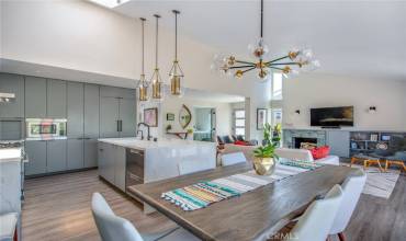 BEAUTIFUL open concept view from dining area onto kitchen area including vaulted ceiling, elegant brass and glass lighting, quartz counter kitchen island, ample cabinet storage space, hidden refrigerator, beautiful stainless-steel appliances and luxury vinyl plank flooring.