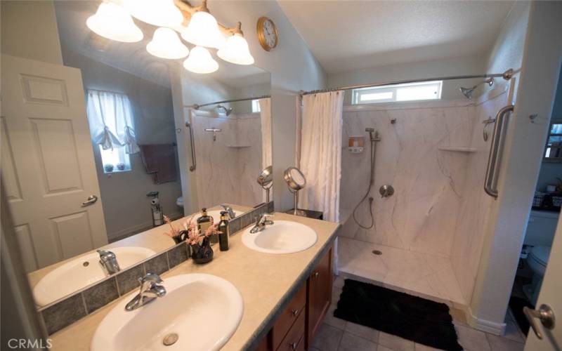 View of the en-suite bathroom in the primary bedroom.  Walk in shower is spacious!  Note hand rail for safety entering into the shower.  Dual sinks and plenty of storage!