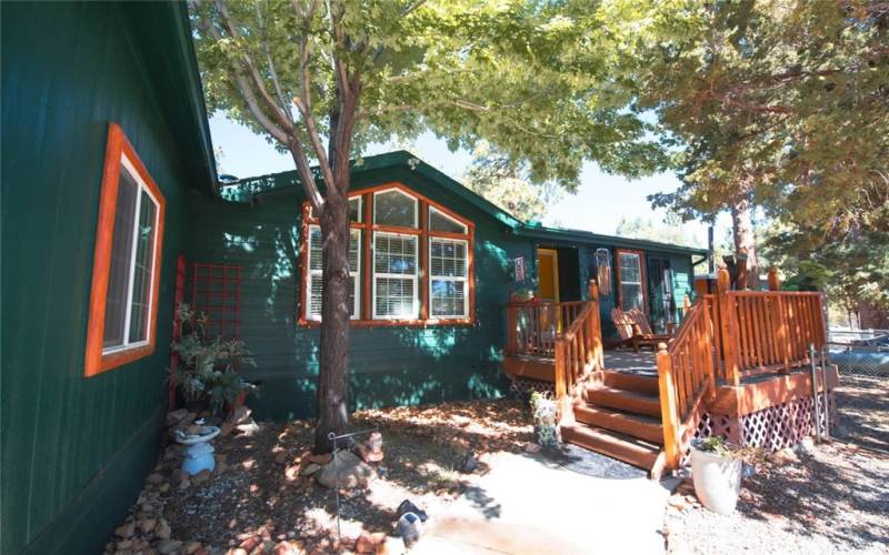 View of the beautifully shaded front porch deck.  Large front window provides an abundance of natural light to the living room.  Also, note there is a window on the left to the garage.  A separate entrance to the right of the main door enters into the primary bedroom.