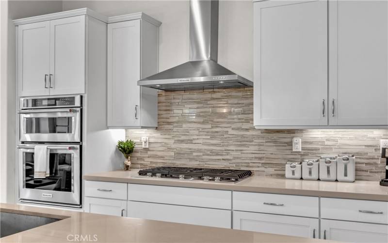 This kitchen offers Quartz countertops, and a tastefully color-coordinated subway tile backsplash, as well as top-of-the-line energy-efficient, stainless steel GE appliances, and a chimney-style range hood.