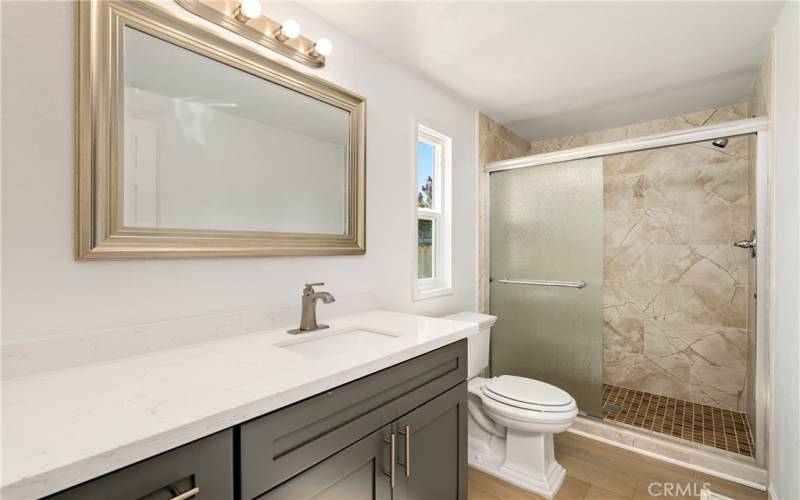 Quartz trimmed vanity, tiled shower with glass doors