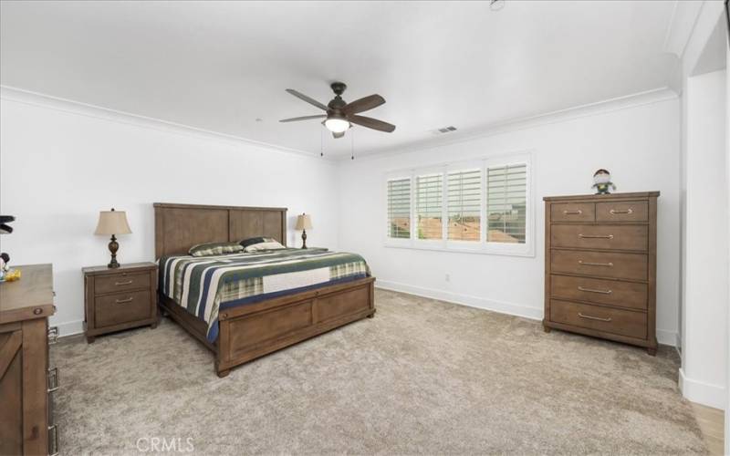 Oversized primary bedroom with custom shutters, ceiling fan.