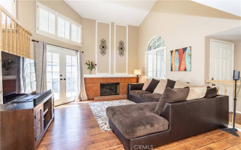 Living room with high ceiling, fireplace, French doors to backyard and front door entry.