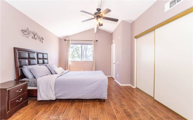 Primary bedroom with high ceiling, closet length of wall, and ceiling fan.