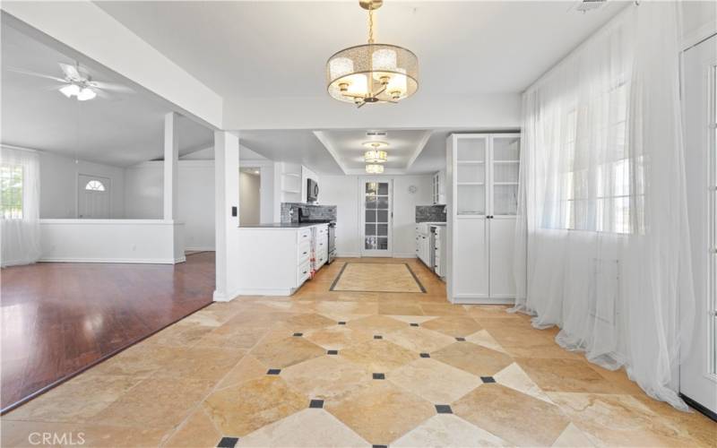 Detailed tile and travertine flooring in kitchen and dining area with 3 modern lights. In the kitchen are two stained glass style modern lights with a silver mesh light for the dining area. Dining area has french doors that open to the back covered patio area